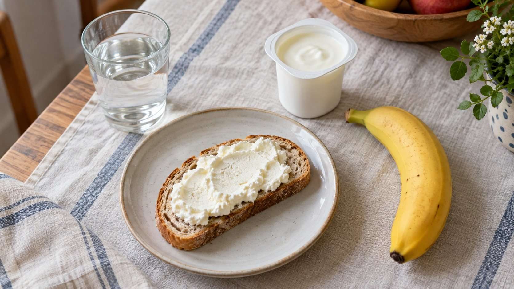 Tostada con queso fresco, plátano, yogur natural y agua sobre una mesa.